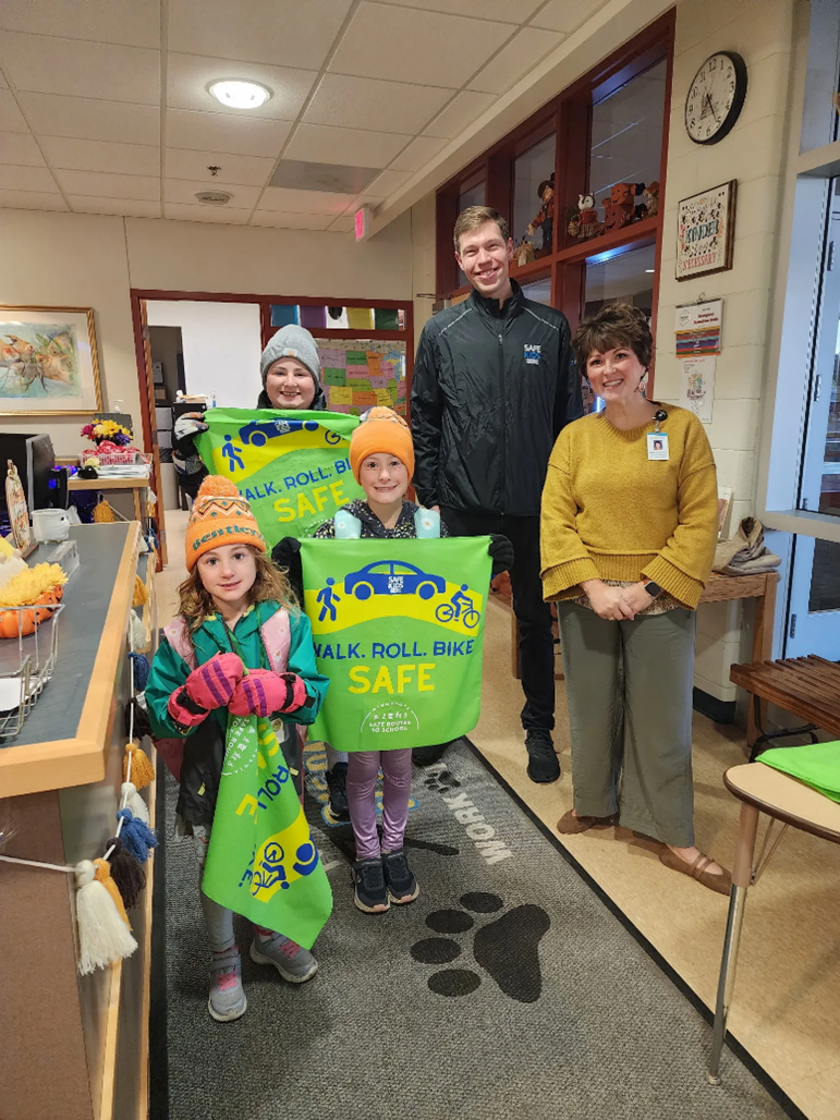 kids and adults holding green banners that show images of bikes, cars and the word safe