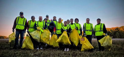 a group of adults wearing safety vests and holding yellow trash bags 